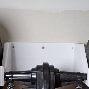 May include: A white plastic wall mount with two screws for mounting a toy truck. The truck has black tires and a black axle.