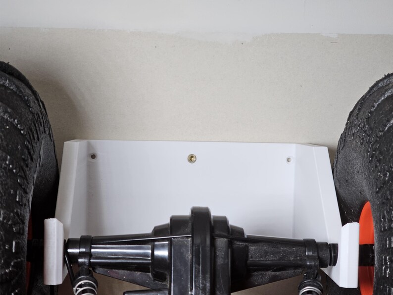 May include: A white plastic wall mount with two screws for mounting a toy truck. The truck has black tires and a black axle.