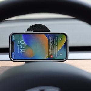 May include: A black phone holder with a smartphone in it. The phone is displaying the time 11:10 and the date Wednesday, July 5. The phone is in a car and the steering wheel is visible in the background.