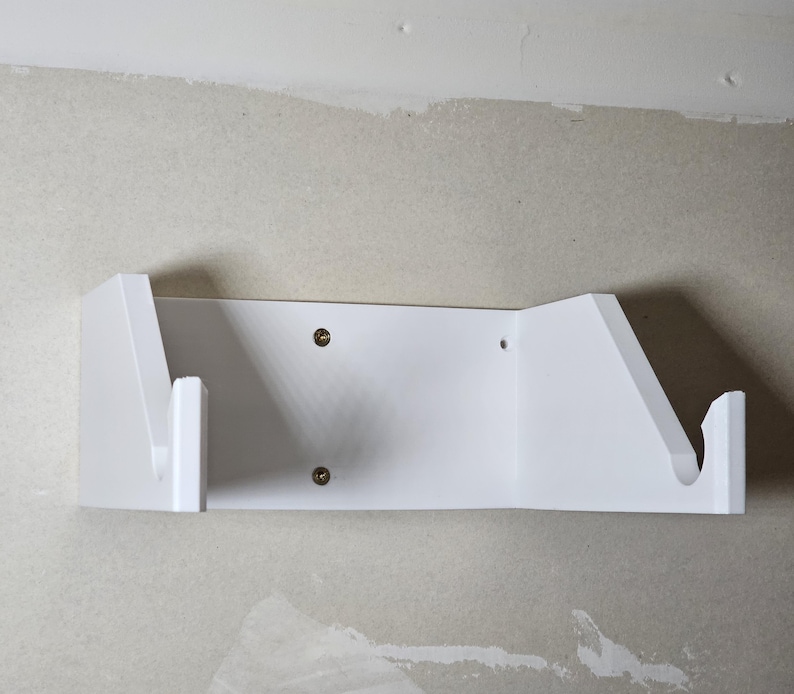 May include: White wall-mounted shelf with two angled supports for holding items. The shelf is made of plastic and has two screw holes on the front.