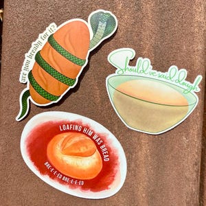 May include: Set of three stickers with food-related puns. One sticker features a loaf of bread wrapped by a green snake with the text "are you bready for it?". Another shows a bowl of dough with the text "Should've said dough". The third sticker has a loaf of bread with the text "LOAFING HIM WAS BREAD".