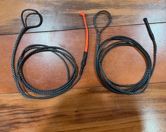 May include: Two black and gray braided ropes with loops at the ends, lying on a wooden surface. One rope has an orange accent and black heat shrink tubing. The ropes are coiled and appear to be new.