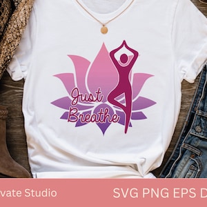 May include: White t-shirt featuring a pink and purple lotus flower design with a woman in a yoga pose. The text "Just Breathe" is written in a pink and purple font.