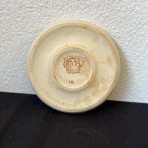 Puede incluir: Parte inferior de un platillo de cer&aacute;mica color crema con un borde elevado. El centro presenta un emblema marr&oacute;n con el texto "BOLESLAWIEC" y "HAND MADE IN POLAND". Tambi&eacute;n es visible el n&uacute;mero "LO".