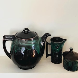 May include: A vintage ceramic tea set with a black and green glaze. The set includes a teapot with a lid, a creamer, and a lidded sugar bowl. The teapot is approximately 25 cm wide. The creamer and sugar bowl have a textured design.