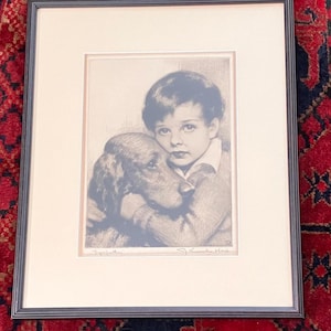 May include: A black and white framed print of a young boy holding a dog. The boy is wearing a collared shirt and the dog is a hound breed. The print is signed "J.C. Leyendecker" and "Sympathy".
