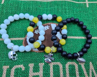 May include: Three beaded bracelets featuring round beads in white, black, and yellow. One bracelet has a silver-toned football helmet charm, another features a silver-toned heart and football charm with the word FOOTBALL, and the third has a football charm.