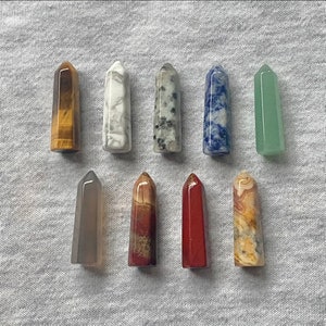 May include: A set of ten crystal points in various colours and patterns, including tiger's eye, white, grey, blue, green, red, and brown. The points are arranged in two rows on a white fabric background.