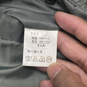 Puede incluir: Una etiqueta blanca con texto japon&eacute;s y s&iacute;mbolos de cuidado, sostenida por una mano. La etiqueta incluye informaci&oacute;n de tallas: pecho 104-112 cm, altura 185-195 cm y X-LA. S&iacute;mbolos de cuidado: lavar a mano, no usar lej&iacute;a y limpiar en seco.