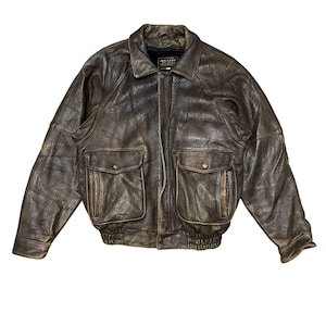 Peut inclure: Une veste bomber en cuir marron avec une fermeture éclair et deux grandes poches à rabat. La veste a une taille et des poignets côtelés.