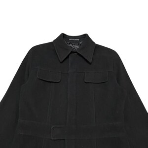 May include: A black coat with a collar, two chest pockets, and a belt. The coat is made of a thick material and has a classic design. The coat is a medium length and appears to be a winter coat.