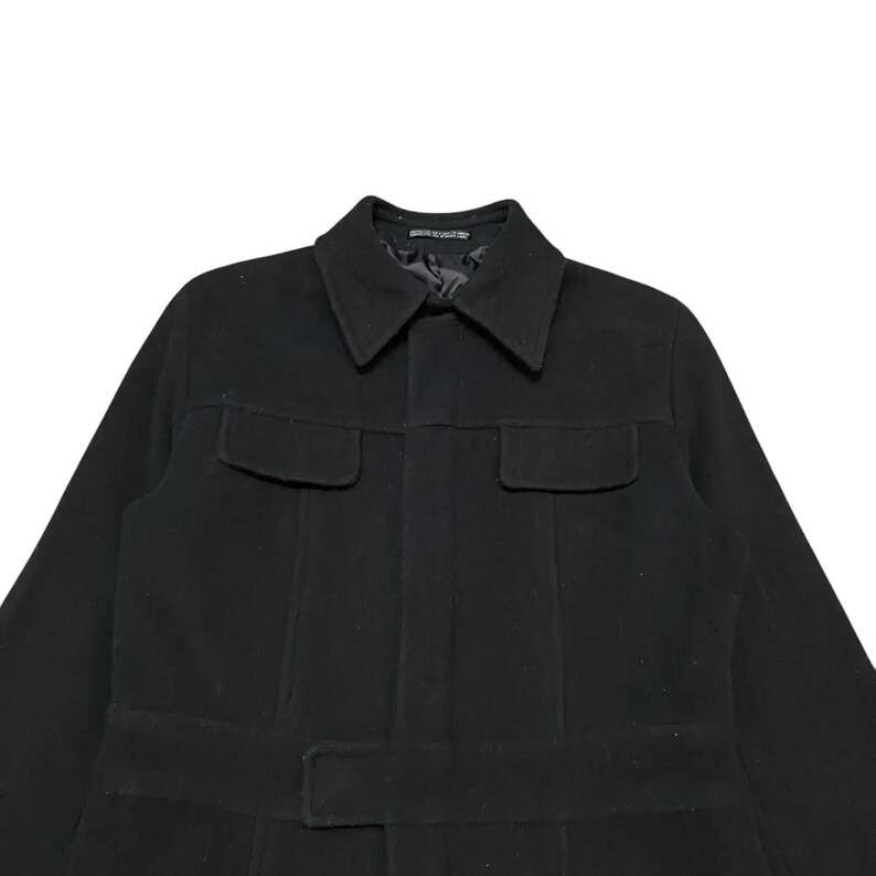 May include: A black coat with a collar, two chest pockets, and a belt. The coat is made of a thick material and has a classic design. The coat is a medium length and appears to be a winter coat.