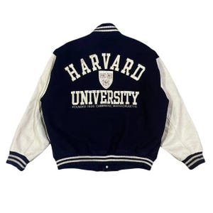 以下が含まれることがあります： 背中に「HARVARD UNIVERSITY」とプリントされた、ネイビーブルーと白のスタジアムジャンパー。ジャケットは白い革の袖とストライプの袖口と裾が付いています。「FOUNDED 1636 CAMBRIDGE, MASSACHUSETTS」の文字が大学名の下に印刷されています。