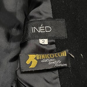 May include: Close-up of black garment labels. The top label reads "IN&Eacute;D" above the number "2". The bottom label features the text "BINICO OCCHI italian textile fashion" with a gold emblem.