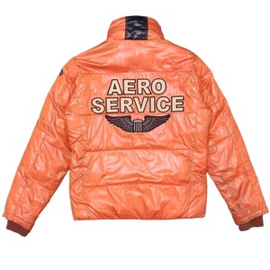May include: Orange puffer jacket with the text "AERO SERVICE" and a winged emblem on the back. The jacket has a black collar and brown cuffs. The jacket is a shiny, quilted material.
