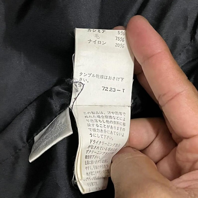May include: A close-up of a clothing tag with Japanese text and percentages for cashmere, wool, and nylon. The tag also includes the number 7223-T.