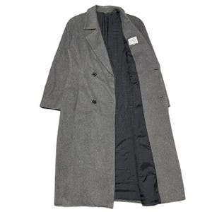 Puede incluir: Un abrigo gris de doble botonadura con cuello de solapa clásico. El abrigo tiene dos filas de botones y un forro negro. Las mangas son largas y el abrigo parece estar hecho de una mezcla de lana. Una etiqueta es visible en el interior.