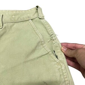 Op de afbeelding: Een lichtgroene cargo broek met een kleine scheur in de zak.