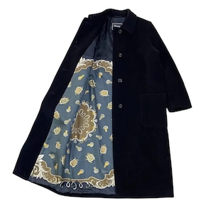 Puede incluir: Un abrigo negro con cuello de solapa y cierre de botones. El forro interior del abrigo presenta un diseño estampado en tonos azules, marrones y dorados. El abrigo tiene un bolsillo en el lado derecho.