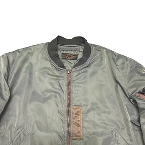 Puede incluir: Chaqueta bomber verde salvia con cuello y pu&ntilde;os de canal&eacute; verde oscuro. La chaqueta presenta cierre de cremallera completa, un parche marr&oacute;n y un peque&ntilde;o parche en la manga. La chaqueta est&aacute; hecha de un material liso y brillante.