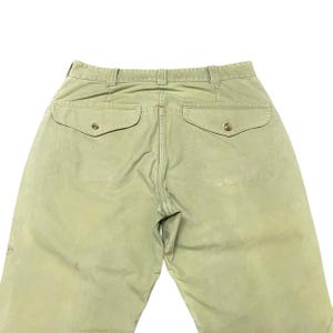 Op de afbeelding: Een lichtgroene cargo broek met twee grote achterzakken en knoopsluitingen.