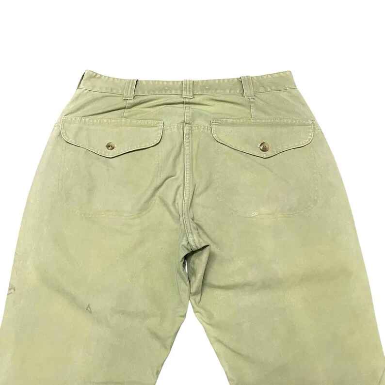 Op de afbeelding: Een lichtgroene cargo broek met twee grote achterzakken en knoopsluitingen.