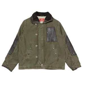 May include: An olive green jacket with a black faux fur collar and leather patches on the elbows and chest. The jacket has a button-up front and a red label on the collar.