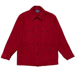 Könnte beinhalten: Ein einfarbig rotes Langarmhemd mit Knopfleiste, spitzem Kragen, zwei Brusttaschen mit geknöpften Klappen und einer zentralen Knopfleiste. Das Kleidungsstück ist innen am Kragen mit einem blauen, rechteckigen Markenetikett versehen.