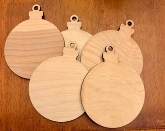 Könnte beinhalten: Eine Sammlung von fünf unfertigen Weihnachtskugel-Ausschnitten aus Holz. Jede Verzierung ist rund mit einer Zwiebelform und einer kleinen Schlaufe zum Aufhängen. Das Holz hat eine helle, natürliche Farbe und sichtbare Maserung.