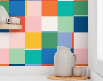 May include: A white ceramic pitcher and a small white ceramic jar with a lid sit on a wooden tray in front of a wall covered in colorful square tiles. The tiles are in shades of blue, green, yellow, orange, pink, and white.