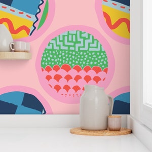 May include: A pink wall with a colourful geometric pattern. The pattern is made up of circles with different designs inside. There is a white jug and a small white jar on a wooden coaster in front of the wall.