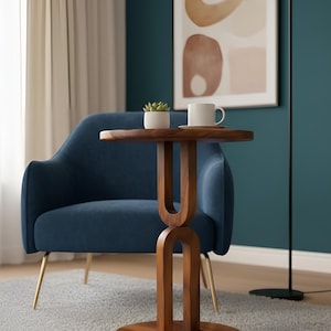 May include: A walnut side table with a circular top and a distinctive arched base. A small white plant pot and a white mug are on the table. A blue armchair with gold legs is in the background. A black floor lamp with a lightbulb is to the right.