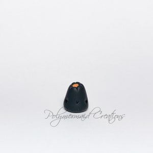 May include: A small black ceramic volcano with an orange top. The volcano has a small opening at the top and a few small holes around the sides.