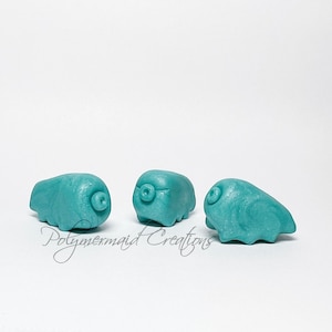 May include: Three teal blue, small, clay figurines of tardigrades, also known as water bears. The figurines are in various poses.