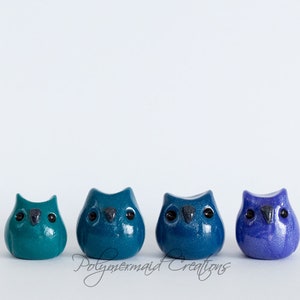 May include: Four small owl figurines in shades of blue and green. The owls are made of polymer clay and have black eyes.