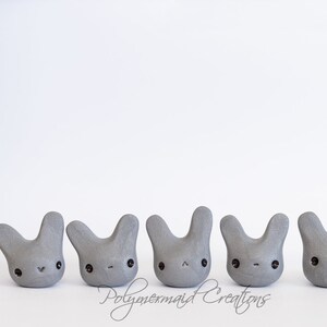May include: Five gray bunny figurines with black eyes and painted details. The bunnies are arranged in a row on a white surface.