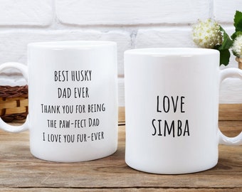 Puede incluir: Dos tazas de cerámica blanca con texto negro. La taza de la izquierda dice "Best Husky Dad Ever. Thank you for being the paw-fect dad. I love you fur-ever." La taza de la derecha dice "Love Simba".