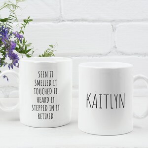 May include: Two white ceramic mugs. One mug has the text "Seen it, smelled it, touched it, heard it, stepped in it, retired." The other mug has the name "Kaitlyn" written on it.