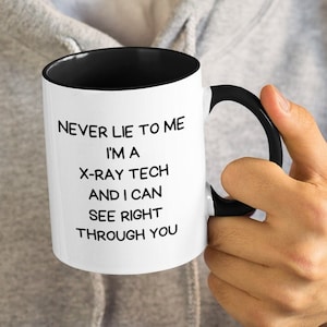 May include: A white coffee mug with a black rim and handle. The mug has black text that reads "Never lie to me I'm a X-ray tech and I can see right through you".