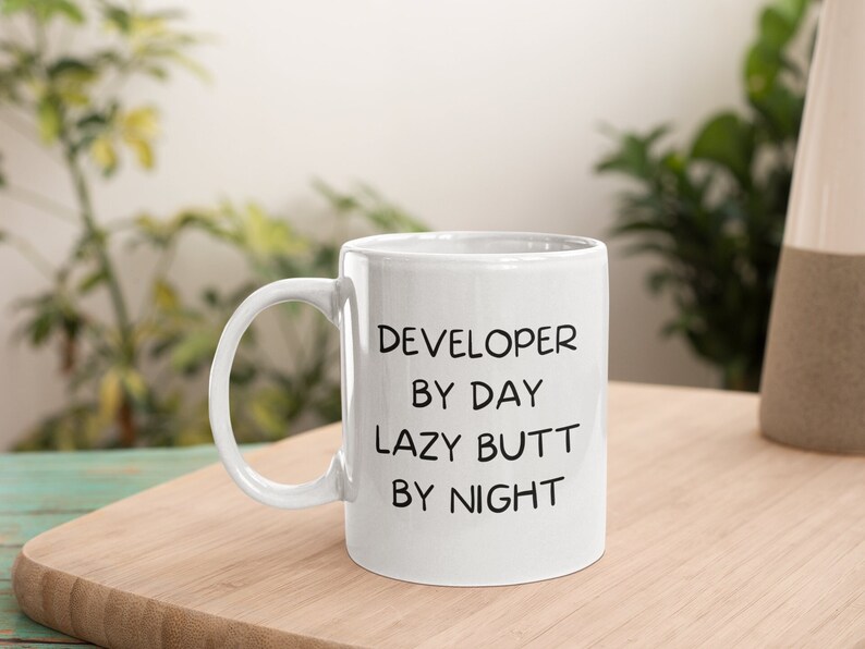 May include: White ceramic coffee mug with black text that reads "DEVELOPER BY DAY LAZY BUTT BY NIGHT".