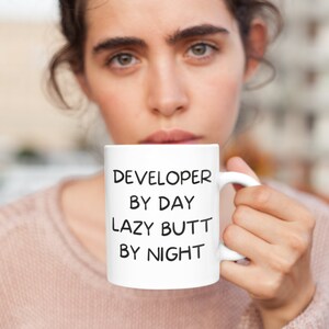 May include: White ceramic mug with black text that reads "DEVELOPER BY DAY LAZY BUTT BY NIGHT".