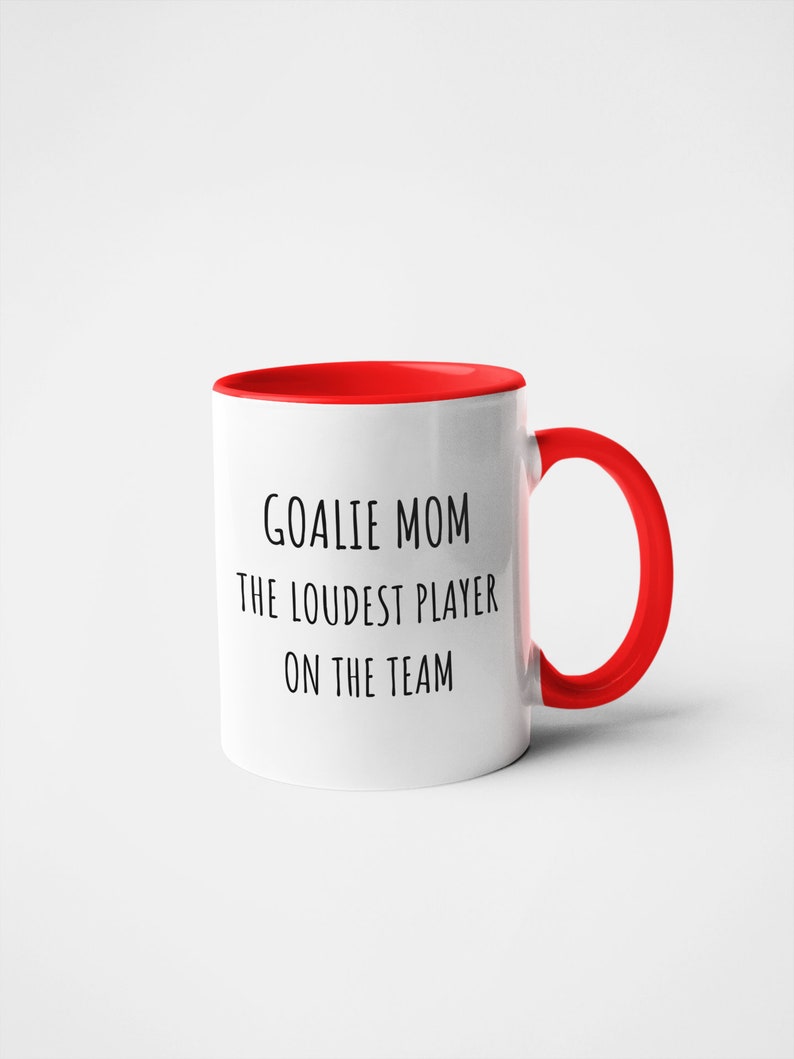 May include: White ceramic coffee mug with a red rim and handle. The mug has black text that reads "Goalie Mom The Loudest Player On The Team."