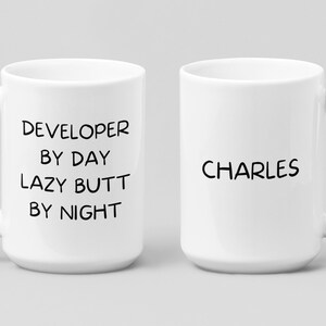 May include: Two white ceramic mugs. One mug has the text "DEVELOPER BY DAY LAZY BUTT BY NIGHT". The other mug has the text "CHARLES".