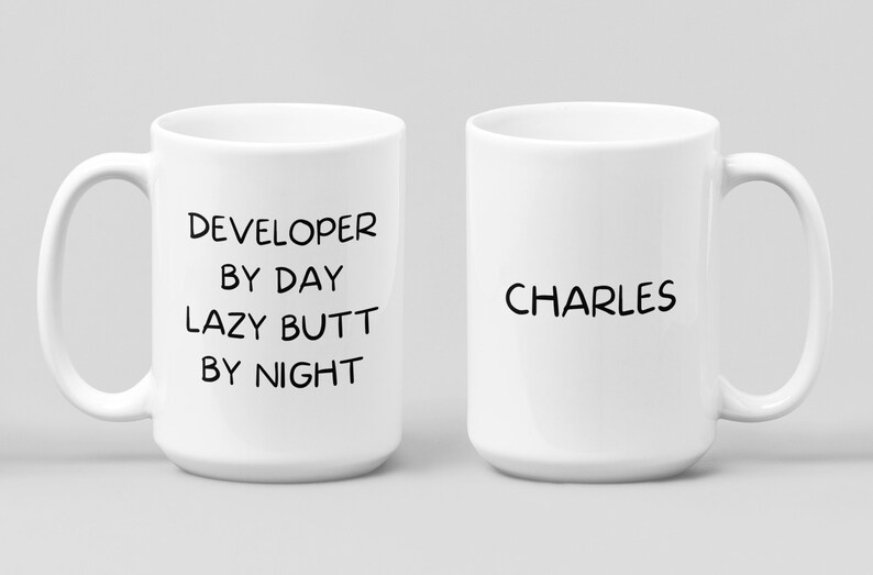 May include: Two white ceramic mugs. One mug has the text "DEVELOPER BY DAY LAZY BUTT BY NIGHT". The other mug has the text "CHARLES".