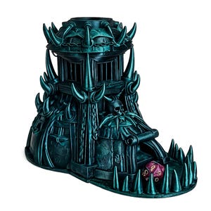 May include: A teal dice tower with a fortress design. The tower has spikes, a skull, and a scroll. A purple twenty-sided die rests in the base. The tower is designed for tabletop gaming and is made of a teal material.