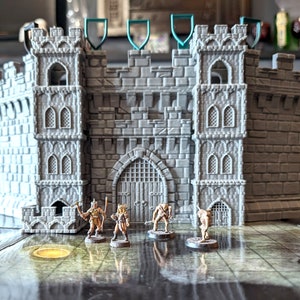 Peut inclure: Un château en plastique gris avec une porte et des tours, avec quatre figurines miniatures debout devant.
