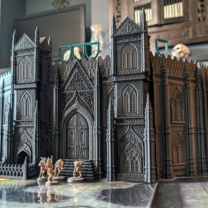 Peut inclure: Un modèle détaillé d'une cathédrale gothique imprimé en 3D en gris foncé avec des détails complexes. Le modèle est posé sur une table avec une surface brun clair. Quatre petites figurines dorées se tiennent devant la cathédrale.