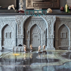 Peut inclure: Un bâtiment en pierre grise avec des portes et des fenêtres cintrées. Le bâtiment est une maquette miniature et est entouré de petites figurines.