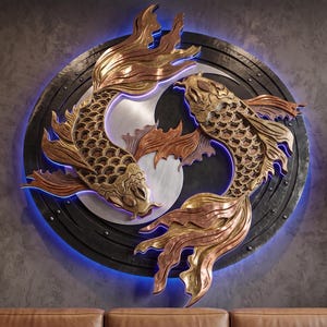 May include: A circular wall sculpture featuring two metallic koi fish in copper and gold tones arranged in a yin-yang formation. The fish are set against a dark, textured circular frame with a glowing blue LED light border that illuminates the edges.