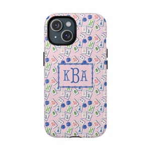 May include: A pink phone case with a repeating pattern of Mahjong tiles and blue floral accents. The case features a blue rectangular frame with the initials "KBA" in the centre. The phone case is designed to fit a smartphone.